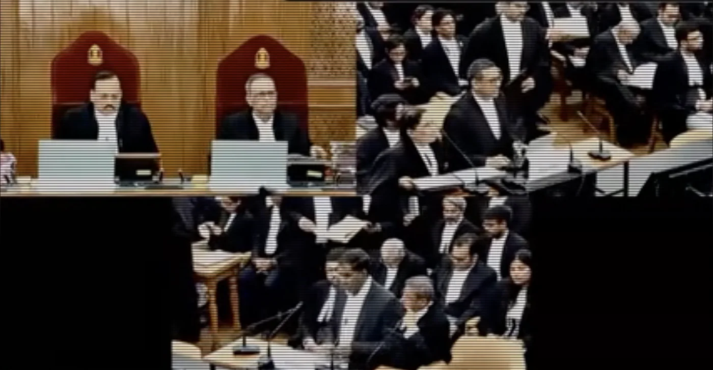 A scan-lined still of a packed courtroom